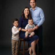 Happy Family Studio Portrait AI Photo Editing Prompt. AI generated studio portrait of a smiling father, mother, young boy, and baby posing together against a dark grey background.
