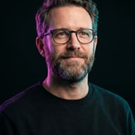 Man in Neon Lighting AI Photo Editing Prompt. AI generated studio portrait of a bearded man wearing glasses illuminated by dramatic magenta and teal rim lights against a dark background.