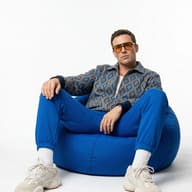 Man in Fashionable Blue Outfit AI Photo Editing Prompt. AI generated studio portrait of a man in a patterned jacket and sunglasses sitting on a blue bean bag.