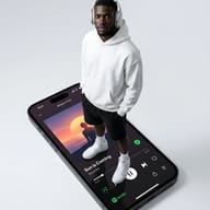 Man on Giant Music Smartphone AI Photo Editing Prompt. AI generated conceptual digital illustration of a man in a white hoodie and headphones standing atop a massive iPhone screen displaying a music player interface.