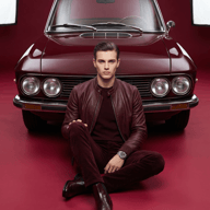 AI generated studio portrait of a stylish man in a burgundy leather jacket and matching apparel sitting cross-legged in front of a classic vintage car.