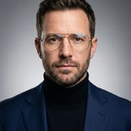 Man in Navy Blazer AI Photo Editing Prompt. AI generated studio portrait of a bearded man wearing wire-rimmed glasses, a black turtleneck, and a navy blue suit jacket against a neutral background.