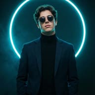 Cinematic portrait of a man in a blazer and sunglasses, framed by a vibrant cyan neon ring. Set against a dark, smoky backdrop with sharp, professional studio lighting.