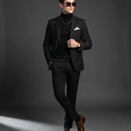 Sharp Man in Black Suit Studio Photography Prompt. AI generated studio portrait of a fashionable man in an all-black suit, turtleneck, and sunglasses posing with polished brown shoes.