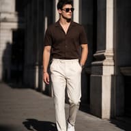 AI generated street style portrait of a handsome man walking outdoors wearing a brown short-sleeve shirt, tailored cream trousers, sunglasses, and white sneakers.